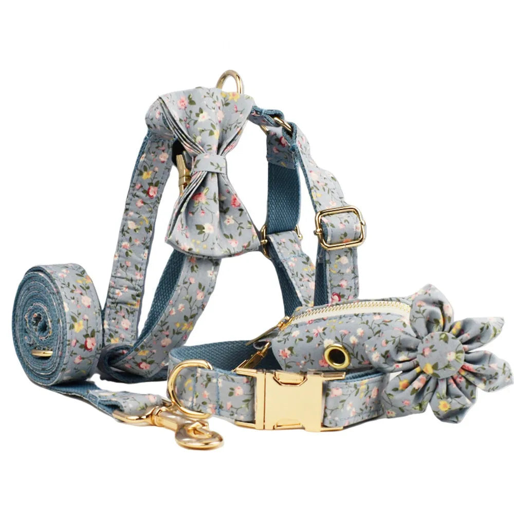 Blue floral pattern dog collar set with matching leash, vest, bow, and poop bag holder on wooden background