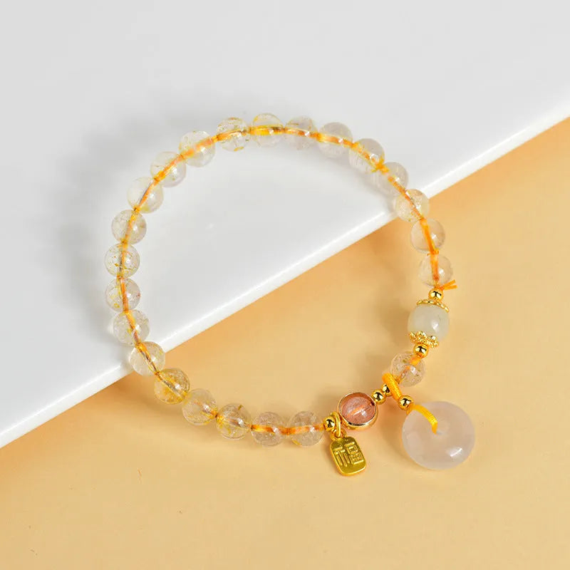Gold rutilated quartz crystal bracelet with a safety buckle and a small rectangular blessing card pendant.