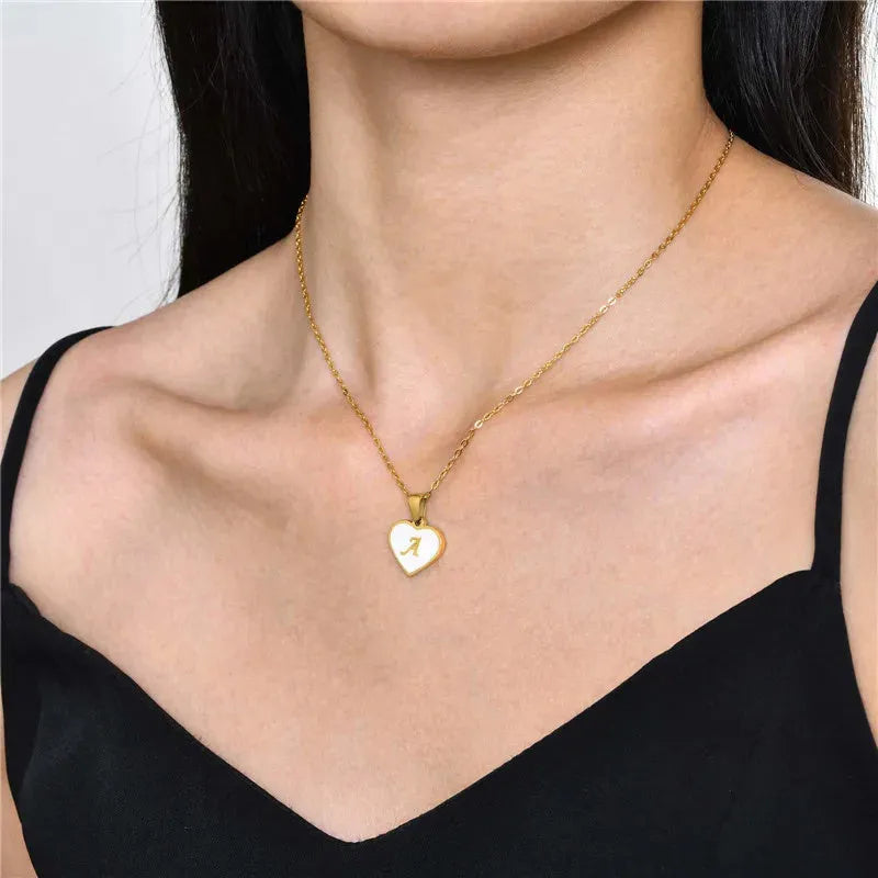 Gold-plated heart-shaped white shell initial necklace on a model, showing the adjustable clavicle chain.