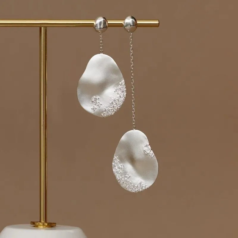 Asymmetric gold and silver floral drop earrings with clear zircon stone detailing on a white background.