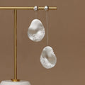 Asymmetric gold and silver floral drop earrings with clear zircon stone detailing on a white background.