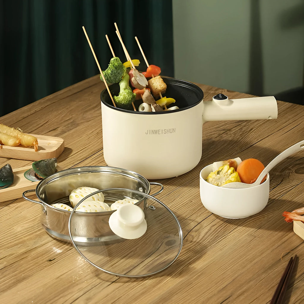 White and green mini electric hot pot cooker with stainless steel body and cooking accessories on a kitchen counter.