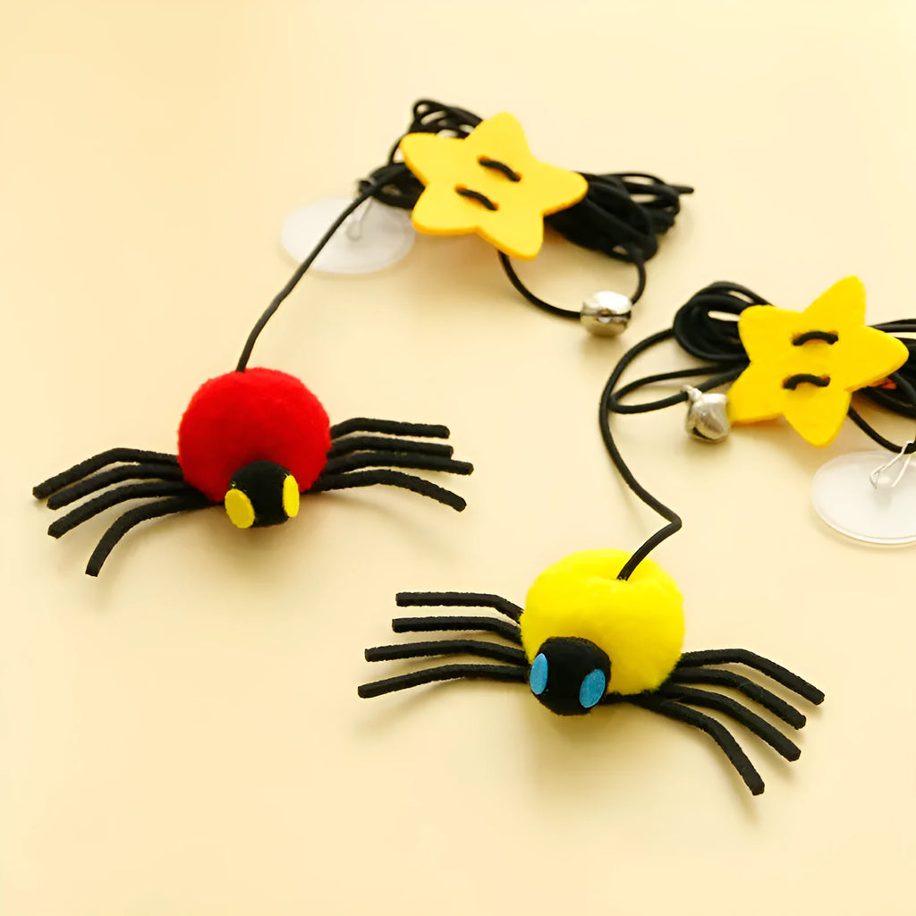Red and yellow elastic rope cat toy hanging from a door, with feathers, a plastic spider, and a bell.